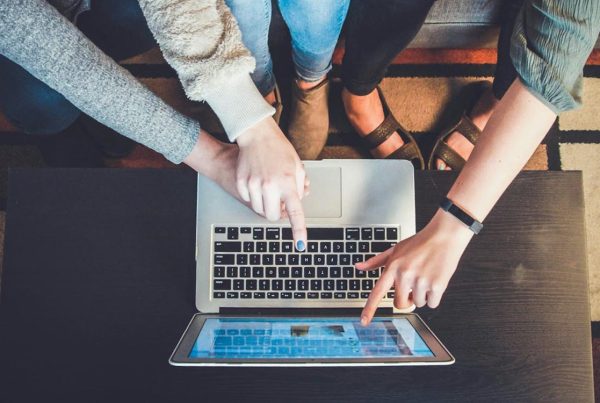 multiple people pointing to social media posts on a laptop